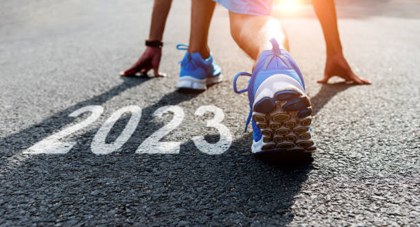 giovane sportivo che si prepara a correre con il numero di capodanno 2023 on the road - il giorno di anno nuovo foto e immagini stock