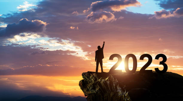 Businessman standing on the top of rock with number 2023 stock photo