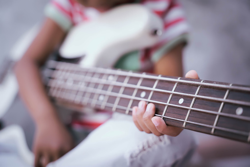 Asian girl child hand holding a 4-string bass guitar with a white color body(focus on fingers).