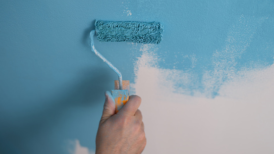 House painter paints wall blue with roller closeup. Repair and painting walls concept