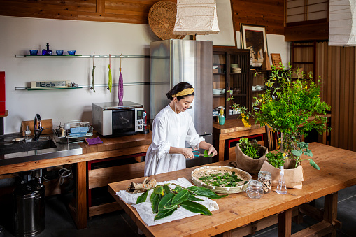 A woman cutting herbs and vegetables in the kitchen.