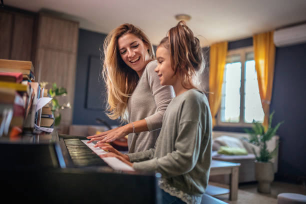 mom and daughter playing the piano in the living room - practicing piano child playing imagens e fotografias de stock