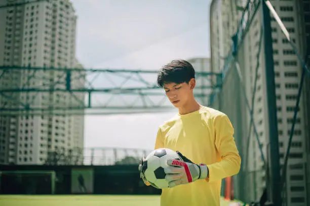 Portrait of a soccer player standing in a soccer field holding a soccer ball.