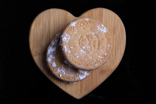 Turkish delight inside biscuits on a wooden heart on a black background with powered sugar.