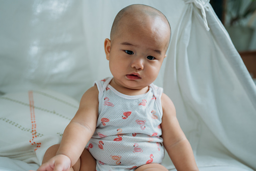 Closed-up image of cute Asian Chinese baby sitting on bed and looking at camera