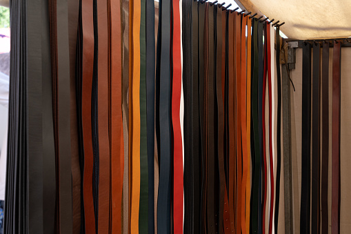 At an outdoor craft fair, a leather goods booth has a display of leather belts in different colors ready to be custom-fitted.