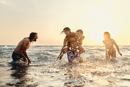 Young cheerful couples having fun during summer vacation in sea at sunset. Copy space.