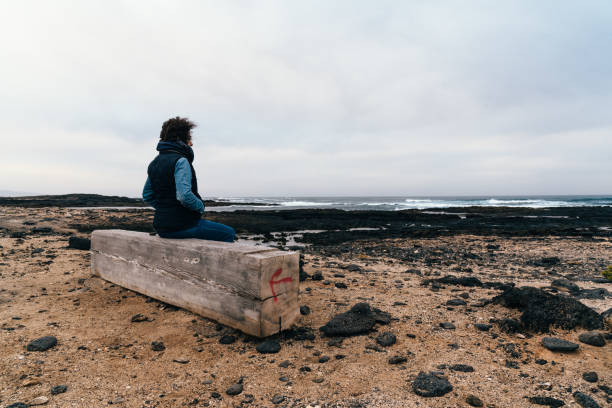 vue arrière d’une femme debout sur un rocher à la plage contre le ciel - volcanic landscape rock canary islands fuerteventura photos et images de collection
