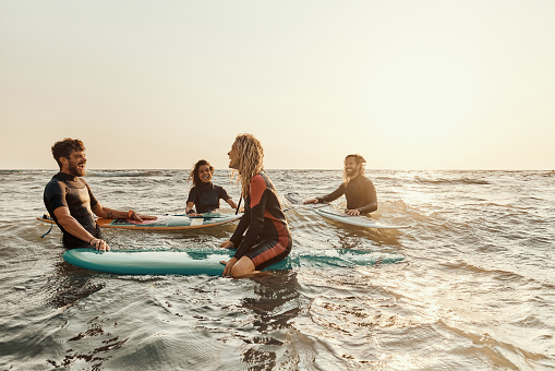 Group of cheerful surfers communicating while enjoying at sea. Copy space.