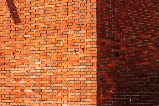Old brick wall with cracks and damage on sunny summer day