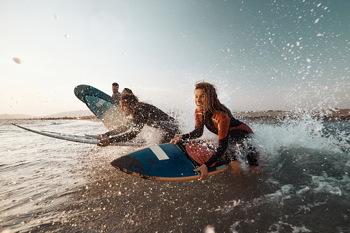 Young carefree woman and her friends having fun while surfing during summer day at sea. Copy space.