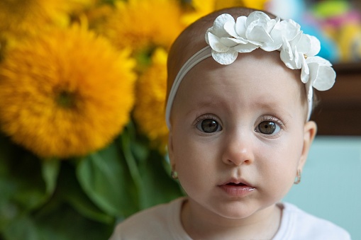Portrait of a baby girl at nine months old. Sunflowers stand behind the back of the child.