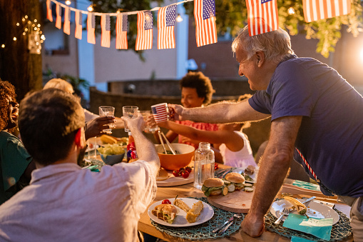 A multi-generation multiracial family having dinner outdoors on an American national holiday