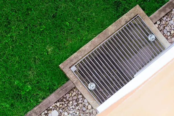 Photo of Stainless Grate of water Drain, gravel, stones and green grass lawn view from above