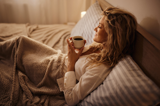 Young smiling woman enjoying during coffee time in bed.