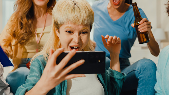 Close-up Group of happy Asian teenage people sit on couch watch cheer sport soccer games together on smartphone. Shouting strike goal excited scream, facial expression concept.