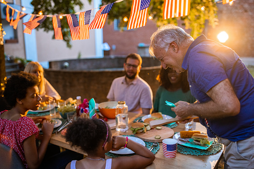 A multi-generation multiracial family having dinner outdoors on an American national holiday