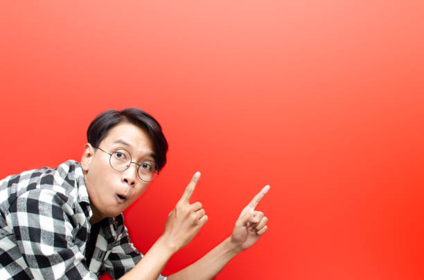 istock asian young man with glasses shocked happily pointing, and presenting something good. 1429931851