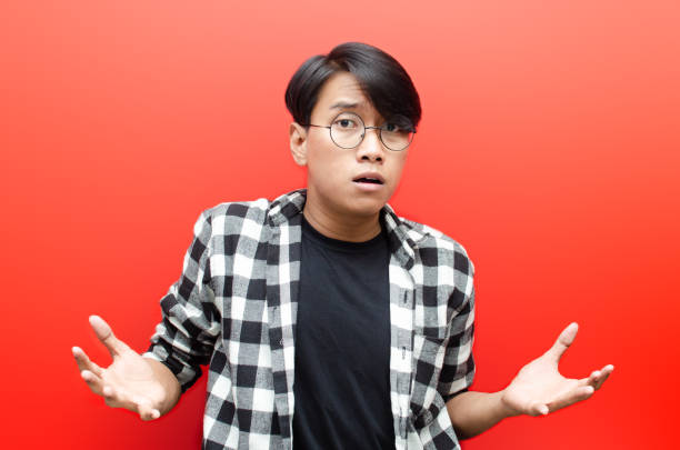 young asian man looks clueless, puzzled, confused, stressed and wondered with hand gesture asking why. isolated over red background. billboard advertisment model concept. - blank expression head and shoulders horizontal studio shot imagens e fotografias de stock