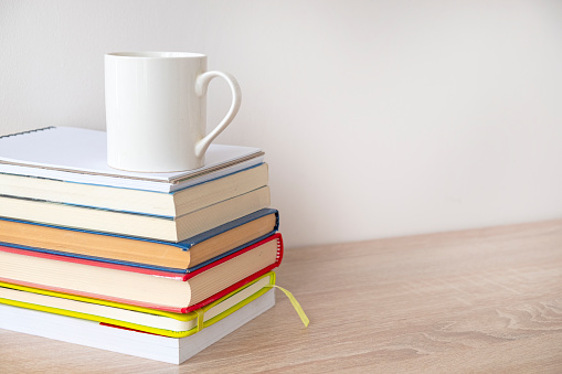 Stack of hardcover books with a white cup of coffee on the top.