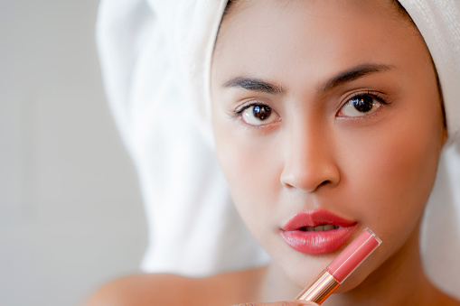Young Women in white towel showing lipstick. Skin care and beauty concept.