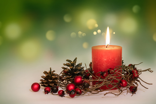 classic christmas decoration with burning red candle on shiny blurred green background, greeting card for holiday season in december