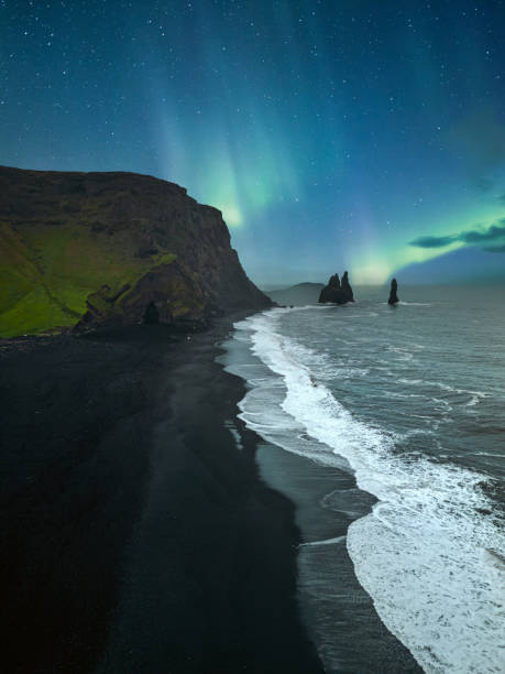 Northern lights over the black sand beach Reynisfjara in Iceland Reynisfjara is a world-famous black sand beach on the South Coast of Iceland. Basalt rocks Reynisdrangar, black volcanic sand and Atlantic ocean in Iceland volcanic landscape stock pictures, royalty-free photos & images