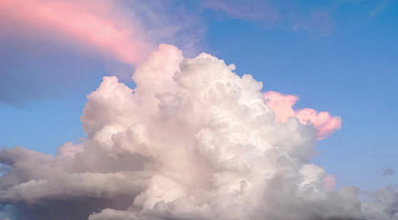 Beautiful cloudscape background, with white and fluffy clouds, pink colored streaks on a soft blue sky. Romance and meditation.