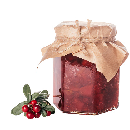 Jar of homemade lingonberry and pear jam with craft paper on lid next to fresh lingonberries isolated on white background. Autumn homemade preparations, stock of food for winter