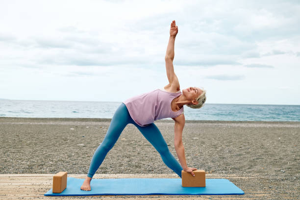 schlanke, gut aussehende frau, die yoga am strand mit hölzernen yogablöcken praktiziert, um beim sport bequemer und einfacher zu üben. - flexibility business gymnastics exercising stock-fotos und bilder