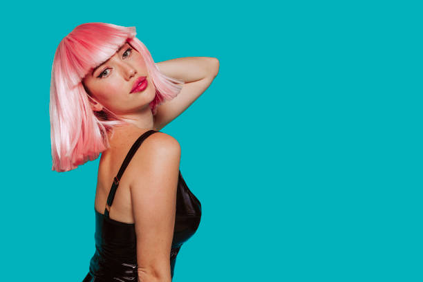 Woman in pink wig posing at studio Profile portrait of a sensual young woman in pink wig, bob haircuts, she touches her neck, make up, big lips, isolated on a blue background. dark pink dress stock pictures, royalty-free photos & images