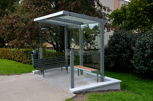 city bus stop. glass shelter with integrated wooden bench. only the roof and the back wall. on the street by the sidewalk in the city. elegant arch, station, platform, lawn, grass, tactile, alopecuroides, miscanthus, subtle, sinensis,