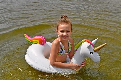 A beautiful little girl swims on an inflatable ring in the river in summer.