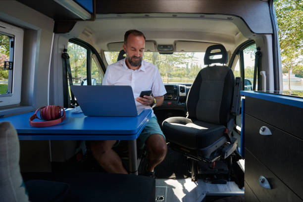 istock Middle-aged man looking at his cell phone while working on his laptop from his camper van. 1429962334