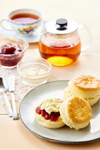 Homemade english scones with cream cheese, strawberry jam and tea on white wooden background