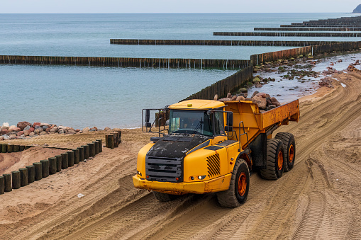 big yellow dump truck is running on the sea coast. a truck carries stones along a sandy beach