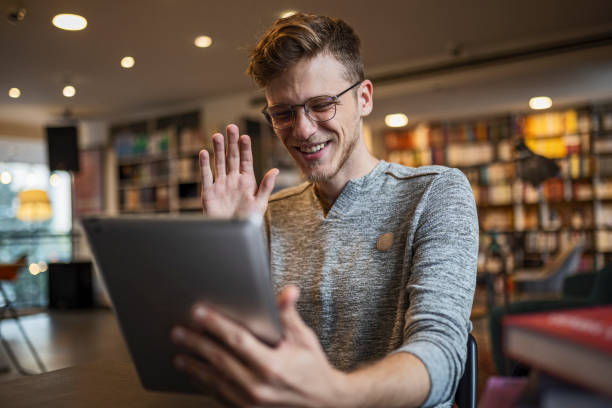 istock Young man sitting in book store using digital tablet for video call 1429963800