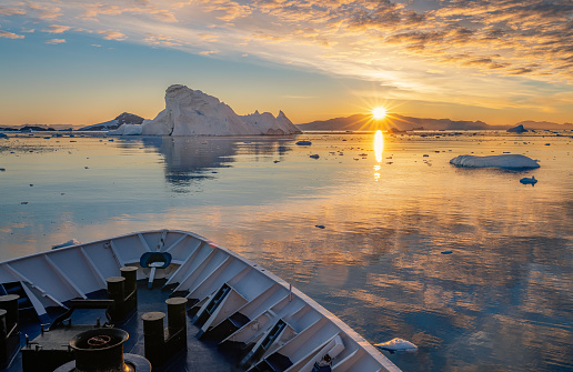 Cruise ship sails through wintry Cierva Cove - a deep inlet on the west side of the Antarctic Peninsula, ringed by Cierva Bay in San Martín Land - Antarctica, during a dramatic sunset / evening sunset.