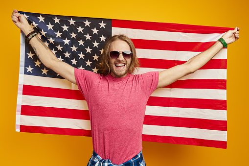 Happy young man carrying American flag while standing against yellow background