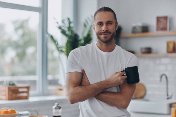 istock Handsome young man holding coffee cup and looking at camera while standing at the kitchen 1429968858