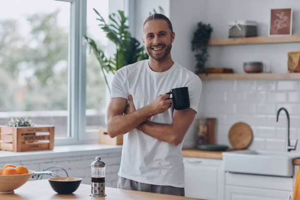 istock Handsome young man enjoying coffee and smiling while standing at the kitchen 1429969557