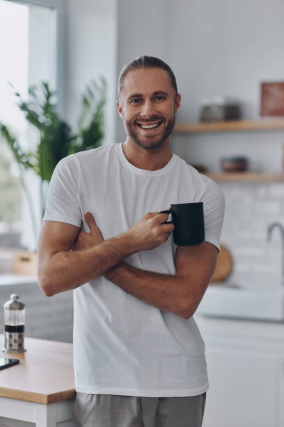 istock Young man enjoying coffee and smiling while standing at the kitchen 1429969560