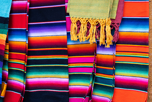 Colorful Mexican serape stripes blankets on street market. Traditional handmade souvenirs from Mexico for sale