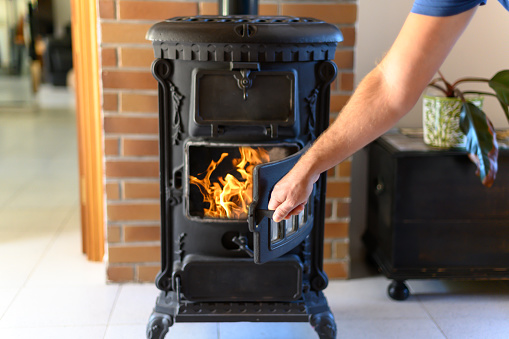 Mature man's hand opening an old burning wood stove. Energy saving concept.