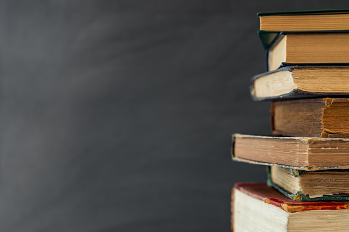 Old book in library with open textbook, stack piles of literature text archive on reading desk, and blur aisle of bookshelves in school study class room background for education learning concept