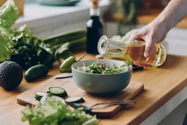 Photo of Close-up of unrecognizable man pouring olive oil into the bowl with fresh salad
