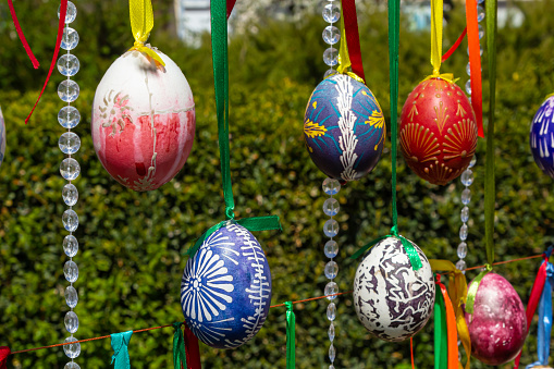 Painted eggs hang from the branches of the Easter tree. The focus is on a yellow egg painted by children by hand. High quality photo