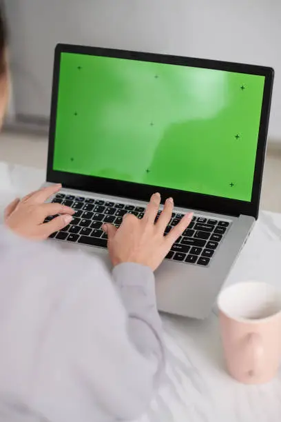 Laptop with black green screen and hands of creative webdesigner typing on keypad while working over new website or application