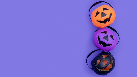 Halloween trick or treat candy theme on purple background with copy space. Three multi-colored pumpkin candy buckets on top of each other. Black, orange and purple Jack'o' Lantern pumpkin pail.