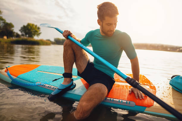 istock Caucasian man, sitting on a standup paddleboard, while oars on the lake 1429986217